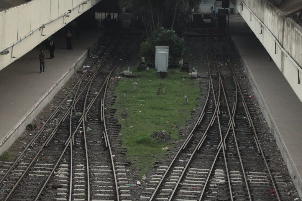 Converging train tracks in an urban station with platforms and people.